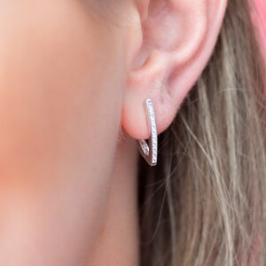 Peut inclure: Une paire de boucles d'oreilles créoles en argent avec une rangée de petits cristaux de zircone cubique transparents.