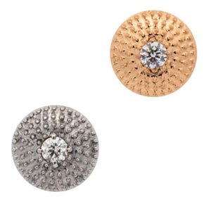 May include: Two round stud earrings. One is gold-toned with a central clear gemstone, and the other is silver-toned with a similar gemstone. Both earrings have a textured, dotted surface around the gemstone.