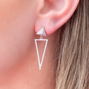 May include: Silver triangle dangle earrings with a small pyramid-shaped top, both covered in clear cubic zirconia stones.