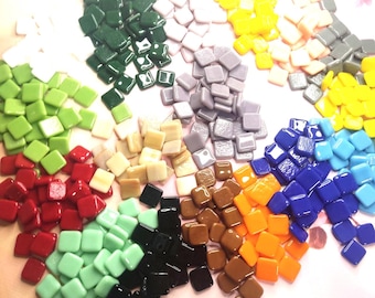 Op de afbeelding: Een verzameling kleine, vierkante mozaïektegels in verschillende kleuren, waaronder groen, rood, geel, blauw en bruin. De tegels zijn in aparte stapels gerangschikt, wat hun glanzende afwerking benadrukt. Ideaal voor knutselprojecten.