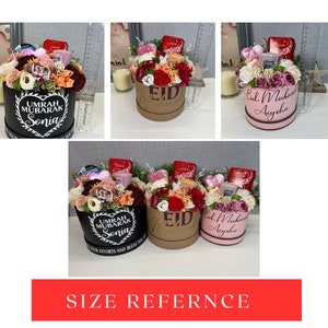 Pode incluir: Uma imagem de refer&ecirc;ncia de tamanho mostrando tr&ecirc;s caixas de presente diferentes cheias de flores, chocolates e outros pequenos presentes. As caixas s&atilde;o decoradas com mensagens personalizadas, incluindo "Eid Mubarak", "Umrah Mubarak" e "Eid".