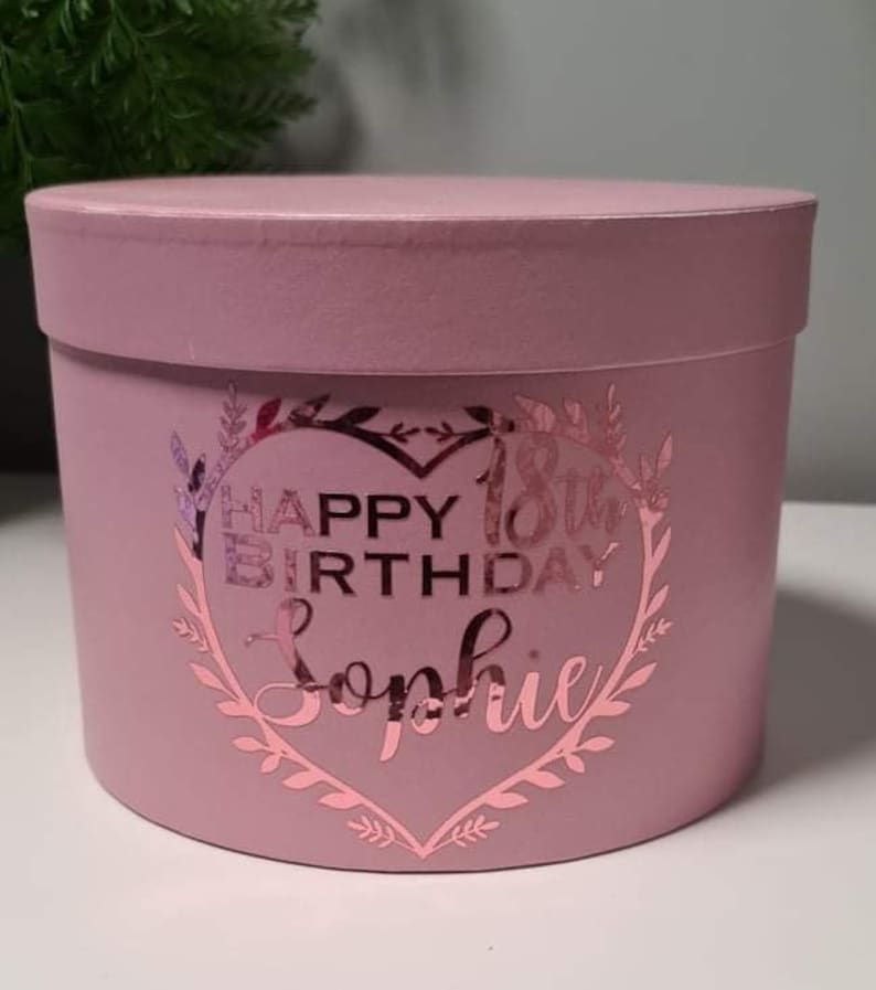 Pu&ograve; includere: Una scatola regalo rotonda rosa con un design in foglia d'oro che dice "Happy 18th Birthday Sophie" a forma di cuore.