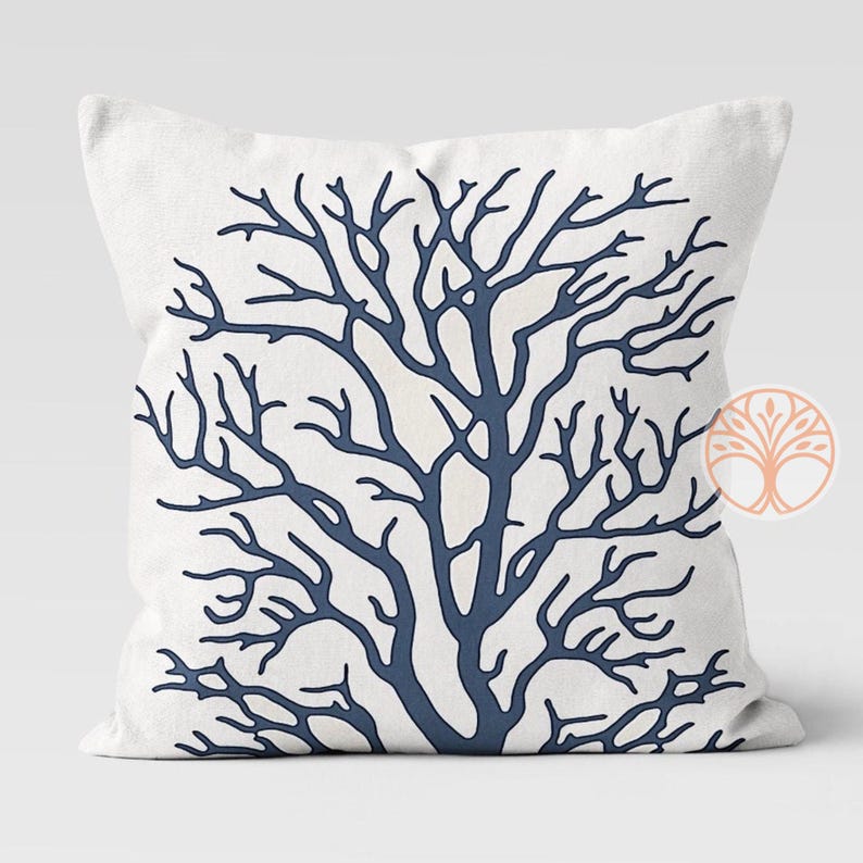 A white throw pillow with a blue silhouette of a coral branch design.