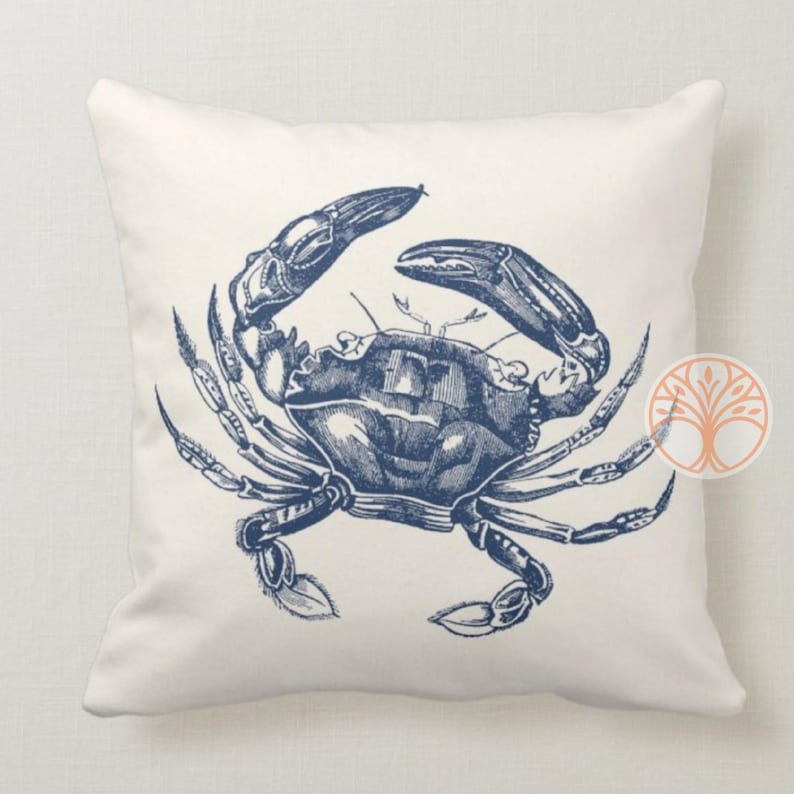 A white throw pillow with a blue illustration of a crab. The crab is facing right and has its claws raised.