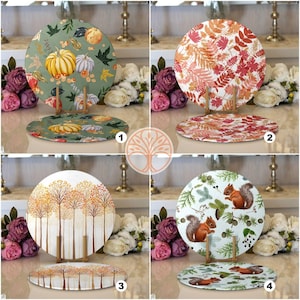 May include: Four round decorative plates with autumn-themed designs. The plates feature pumpkins, leaves, trees, and squirrels. The plates are displayed on stands.