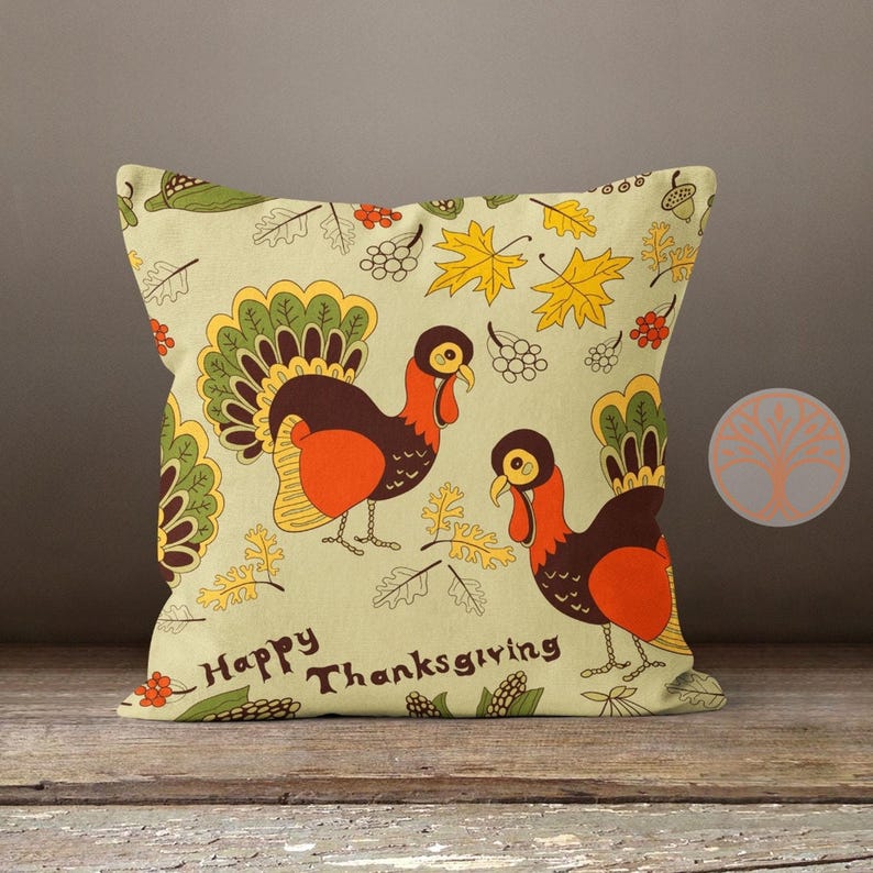 Może przedstawiać: Dekoracyjna poduszka z motywem Dnia Dziękczynienia. Poduszka ma jasnozielone tło z dwoma indykami, jesiennymi liśćmi i tekstem "Happy Thanksgiving".