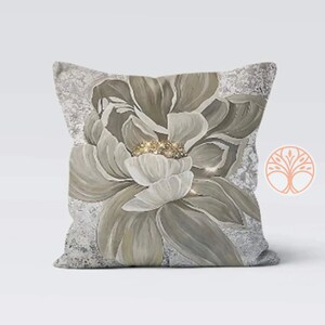 A decorative throw pillow with a large, white flower with gold accents on a gray background. The flower is painted in a realistic style and has a soft, romantic feel.