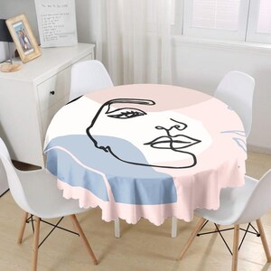 May include: Round pink and blue tablecloth with a black line drawing of a face. The tablecloth has a scalloped edge.
