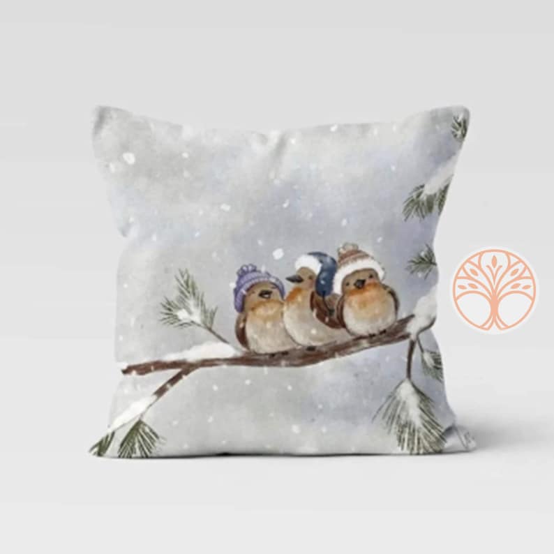 Three birds wearing purple and blue knit hats are perched on a snowy pine branch. The birds are brown with white bellies and are looking to the right. The background is a watercolor painting of a snowy winter scene.