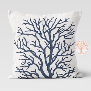 A white throw pillow with a blue silhouette of a coral branch design.