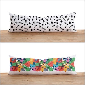 Op de afbeelding: Twee decoratieve kussens. Het eerste kussen heeft een witte achtergrond met een zwart, herhalend patroon van visgraten en potafdrukken. Het tweede kussen heeft een witte achtergrond met een kleurrijk, herhalend patroon van schelpen, zeesterren en zeewier.