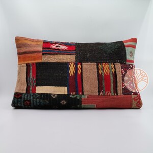 Può includere: Un cuscino rettangolare in patchwork con una varietà di colori e motivi, tra cui rosso, nero, marrone e verde. Il cuscino è realizzato in tessuto tessuto e ha una superficie leggermente strutturata.