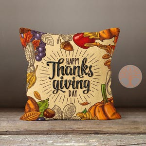 Może przedstawiać: Poduszka dekoracyjna w stylu Dnia Dziękczynienia z beżowym tłem i vintage ilustracją jesiennych zbior&oacute;w. Tekst "Happy Thanks Giving Day" jest nadrukowany czarnymi literami.
