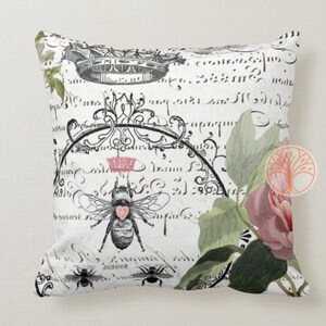 May include: A white pillow with a black and white floral design featuring a bee with a pink heart. The background is a white and black script.