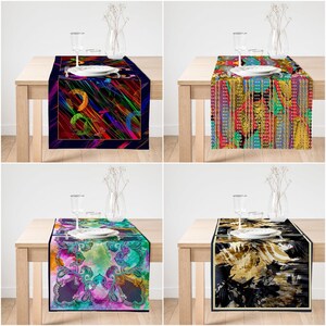 May include: Four different table runners with colorful abstract designs. Each runner is displayed on a wooden table with a glass of water and a plate.