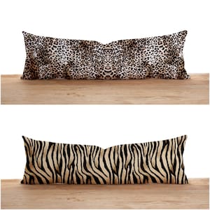 May include: Two long decorative pillows. The top pillow has a leopard print pattern in shades of brown, black, and cream. The bottom pillow has a zebra stripe pattern in black and tan. Both pillows are rectangular.