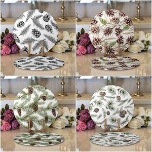 May include: Four white ceramic plates with a pine cone and pine needle design. The plates are on a wooden stand and are surrounded by white flowers.
