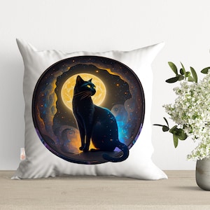 May include: A white throw pillow with a black cat sitting in front of a full moon. The moon is surrounded by a swirling galaxy of stars and nebulae.