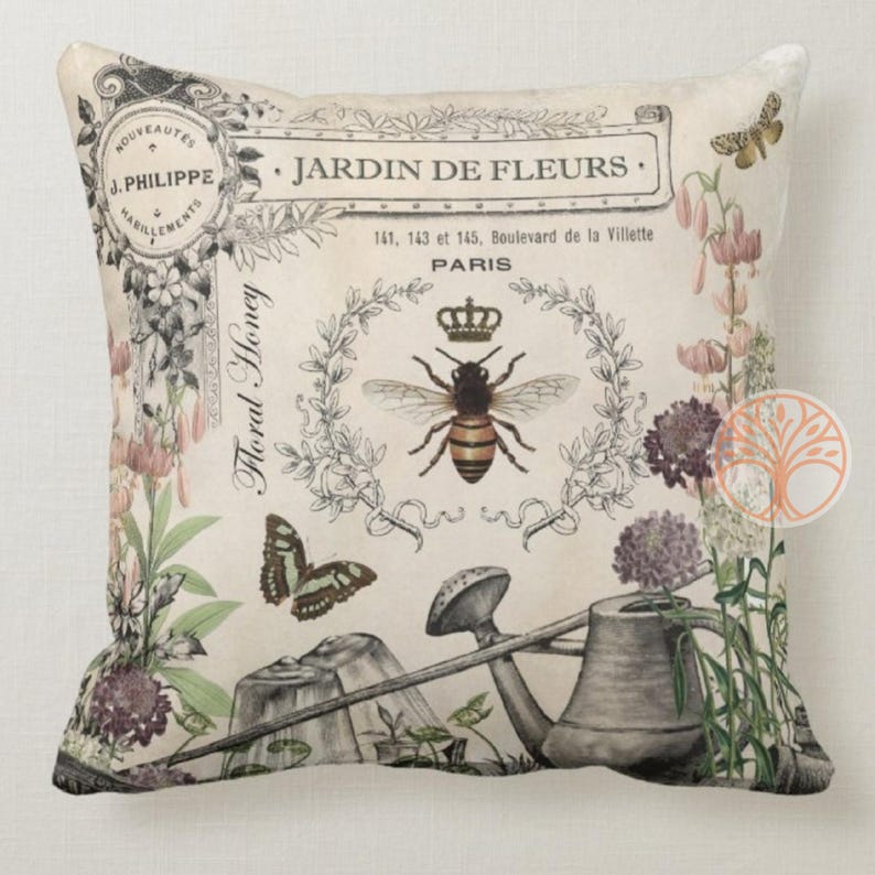 May include: A decorative pillow featuring a vintage floral design with a bee, butterfly, and watering can. The pillow has the text "JARDIN DE FLEURS" and "Floral Honey" printed on it.
