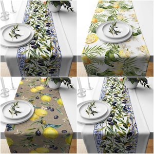 May include: Four different table runners with various designs featuring lemons, olives, and leaves. The table runners are all white with a blue and white border. The designs are all watercolor style.