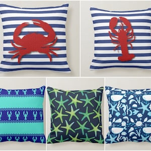 May include: Set of four decorative throw pillows featuring nautical themes. One pillow has a red crab on a blue and white striped background. Another pillow has a red lobster on a blue and white striped background. One pillow has a blue and turquoise striped background with a repeating pattern of red lobsters. The last pillow has a dark blue background with a repeating pattern of green starfish and white sea creatures.