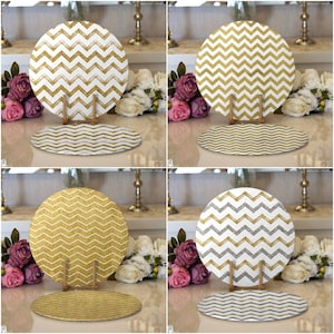 Op de afbeelding: Vier ronde placemats met een chevron-patroon in goud en zilver. De placemats liggen op een witte tafel met een vaas met bloemen op de achtergrond.