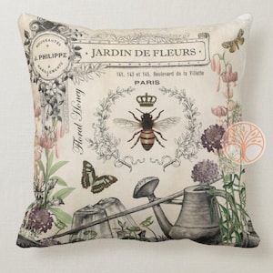 May include: A decorative pillow featuring a vintage floral design with a bee, butterfly, and watering can. The pillow has the text "JARDIN DE FLEURS" and "Floral Honey" printed on it.