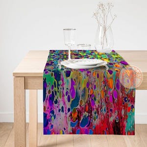 Könnte beinhalten: Ein farbenfroher Tischläufer mit einem Marmormuster in Blautönen, Grün, Lila, Gelb, Orange und Rot. Der Läufer liegt auf einem Holztisch mit einem Wasserglas und einem Teller.