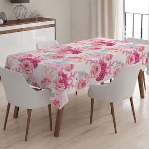 May include: A white tablecloth with a pink and blue floral pattern. The tablecloth is laid on a wooden table with four white chairs.
