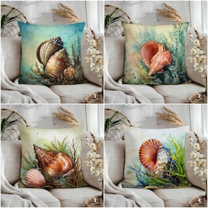 Może przedstawiać: Cztery dekoracyjne poduszki z motywami muszli. Każda poduszka przedstawia inny akwarelowy obraz muszli i roślin wodnych w odcieniach brązu, pomarańczy, błękitu i zieleni. Poduszki są wystawione na kremowej sofie.
