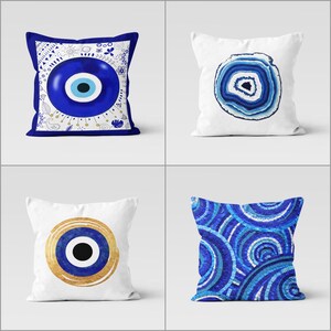 May include: Four decorative throw pillows with blue and white designs. One pillow features a blue eye symbol, another a blue agate slice, a third a gold and blue eye, and the last a mosaic of blue circles.