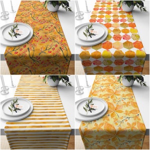 May include: Four different table runner designs with autumnal themes. The designs include a pattern of small red berries and branches, a geometric pattern of orange and yellow hexagons, a pattern of yellow and orange stripes, and a pattern of yellow and orange leaves.
