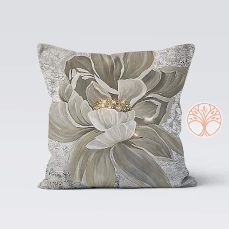A decorative throw pillow with a large, white flower with a gold center on a gray background. The flower is stylized and has a soft, watercolor-like appearance.