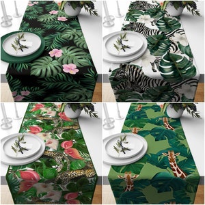 May include: Four table runners with different tropical designs. The designs include palm leaves, jungle animals, and flowers. The table runners are all green, black, and white.