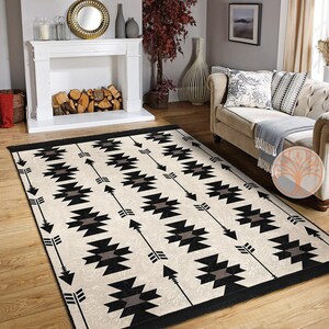 May include: A black and white geometric rug with a repeating pattern of arrows and diamonds. The rug has a cream background and black accents. The rug is laid out on a hardwood floor in a living room setting.