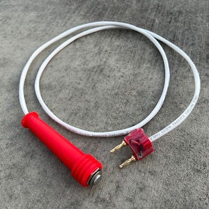 May include: A white cable with a red handle and gold-tipped connectors. The cable is labeled "AUDIO CABLE  W/D10  CABLE  WHITE  2x0.50SQ  E200472  PHOTO CELL".