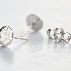 May include: A pair of silver stud earrings with a hammered, round, textured design. The earrings are shown on a white surface.