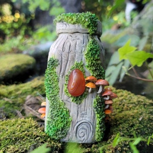 May include: A ceramic bottle shaped like a tree trunk with moss and mushrooms. The bottle has a red agate stone embedded in the side.