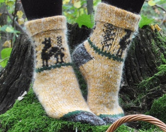 May include: A pair of handmade, yellow wool socks with a deer design, green and gray accents. The socks are displayed on a moss-covered tree stump, with a basket of yarn and knitting needles in the foreground. The scene is set outdoors.