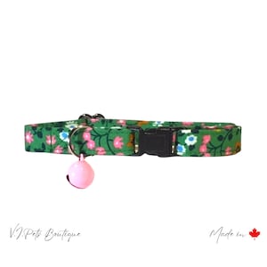 May include: Green cat collar with a pink floral pattern and a pink bell. The collar has a black buckle and is made in Canada.