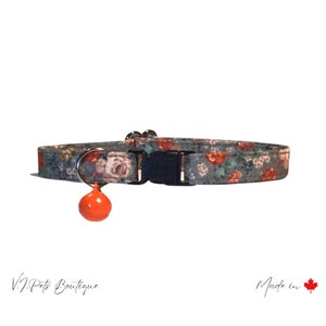 May include: A gray floral cat collar with a bell. The collar has a black buckle and a silver ring. The bell is orange.