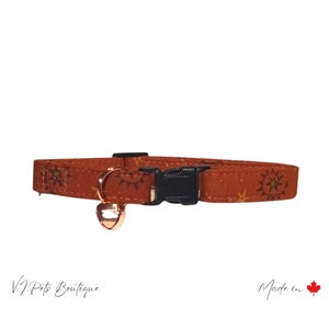 May include: A brown cat collar with a gold bell and a black buckle. The collar has a pattern of small stars and suns. The text "Made in Canada" is visible in the bottom right corner of the image.