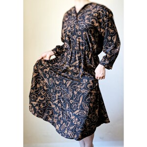 May include: A black midi dress with long sleeves and a brown abstract print of various shapes. The dress has a cinched waist and a flowing skirt.