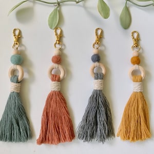 Puede incluir: Cuatro llaveros de borla coloridos con anillos y cuentas de madera. Las borlas son en tonos de verde, naranja, gris y amarillo.