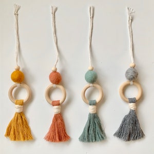 May include: Four wooden ring toys with colorful felt balls and tassels. The rings are made of natural wood and the tassels are made of yarn. The colors of the felt balls are yellow, orange, green, and gray. The tassels are yellow, orange, green, and gray.