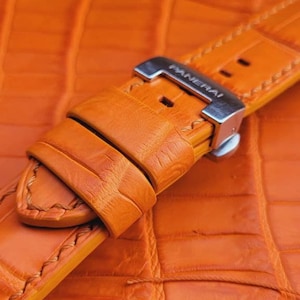 May include: Orange leather watch strap with a silver buckle that says "PANERAI".