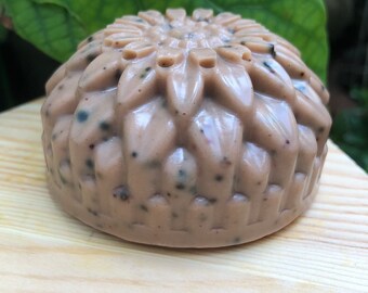 Puede incluir: Una pastilla de jabón beige y marrón con un diseño en forma de flor y motas negras por todas partes. El jabón está sobre una superficie de madera.