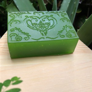 May include: A green bar of soap with a decorative heart design. The soap is on a wooden surface.