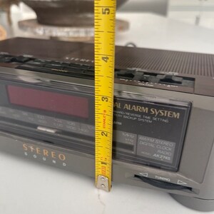 Pu&ograve; includere: Un radio digitale stereo AM/FM grigio e nero con un display digitale rosso. La radio ha un numero di modello AK2745 e dispone di una manopola di sintonizzazione e un sistema di allarme.