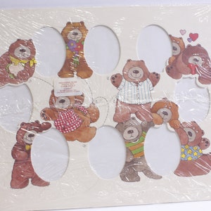May include: A white cardstock sheet with 10 oval cutouts, each featuring a different illustration of a brown bear wearing various outfits. The bears are holding items like flowers, a ball of yarn, and a heart. The text "Friends Ring Bears Party Favors" is printed on the card.